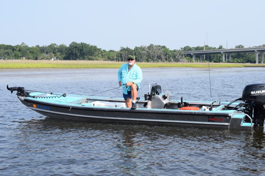 Angler standing on a boat near a bridge with marsh in the background